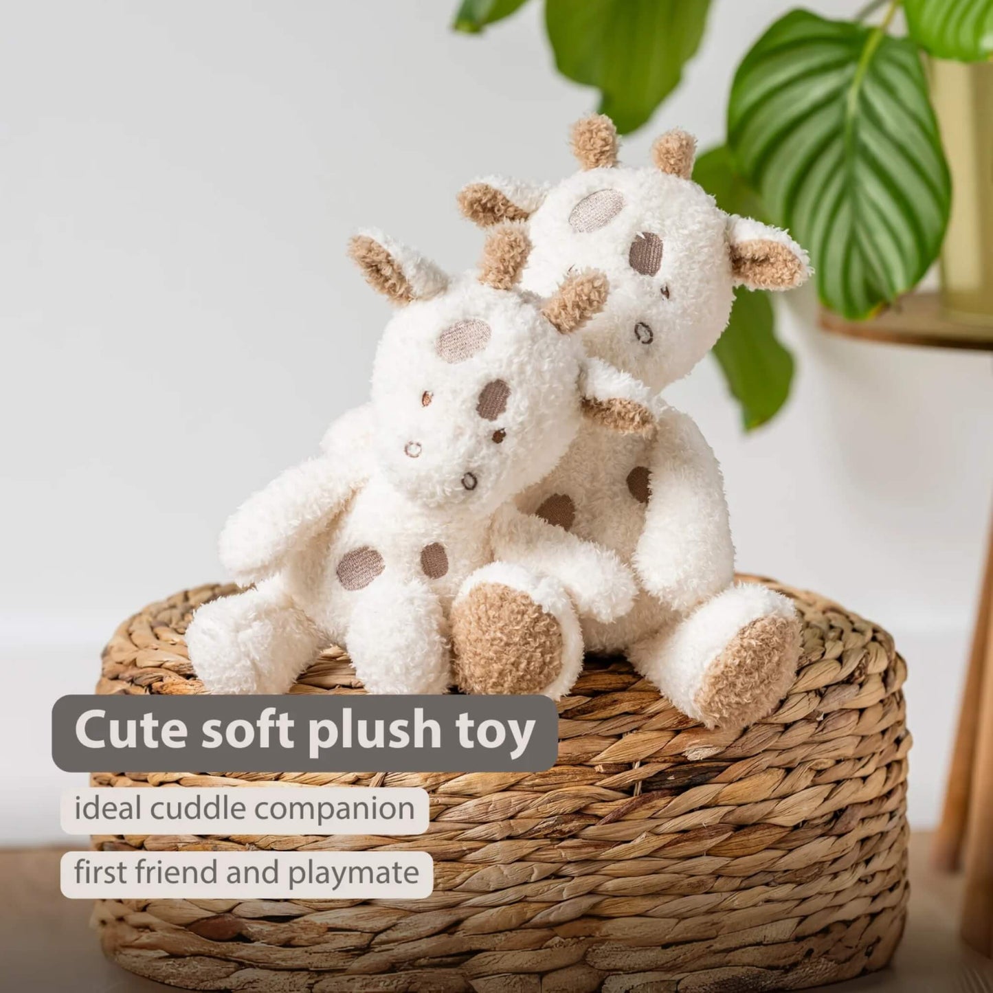 Two soft giraffe plush toys resting together on a woven basket, with on-image text reading “Cute soft plush toy”, “ideal cuddle companion” and “first friend and playmate.” Plush bodies appear cream with brown spots and textured horns, set against a neutral backdrop.