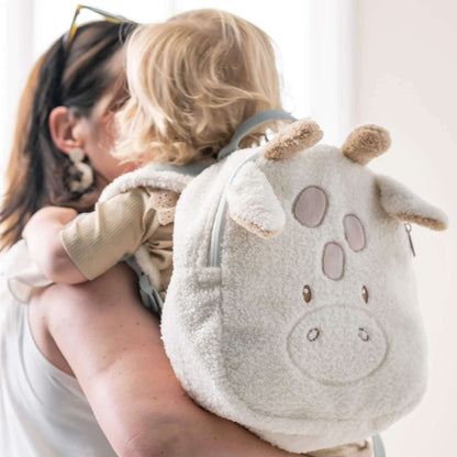 A soft giraffe-shaped toddler backpack worn by a small child, showing plush ears, small horns and light grey shoulder straps.