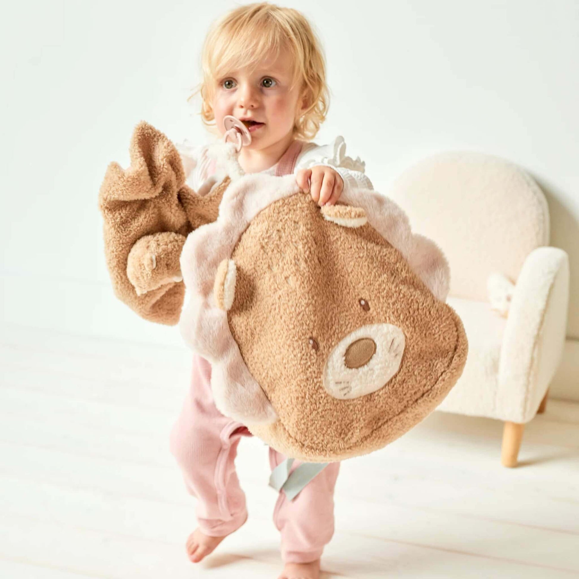 A toddler holding an open lion-shaped backpack, revealing the soft fabric and spacious interior while standing near a small chair.