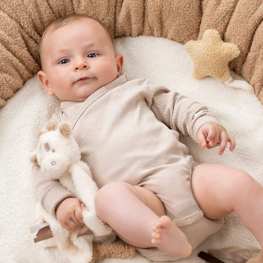 Baby in beige outfit cuddling a Giraffe Doudou comfort blanket on soft white blanket.