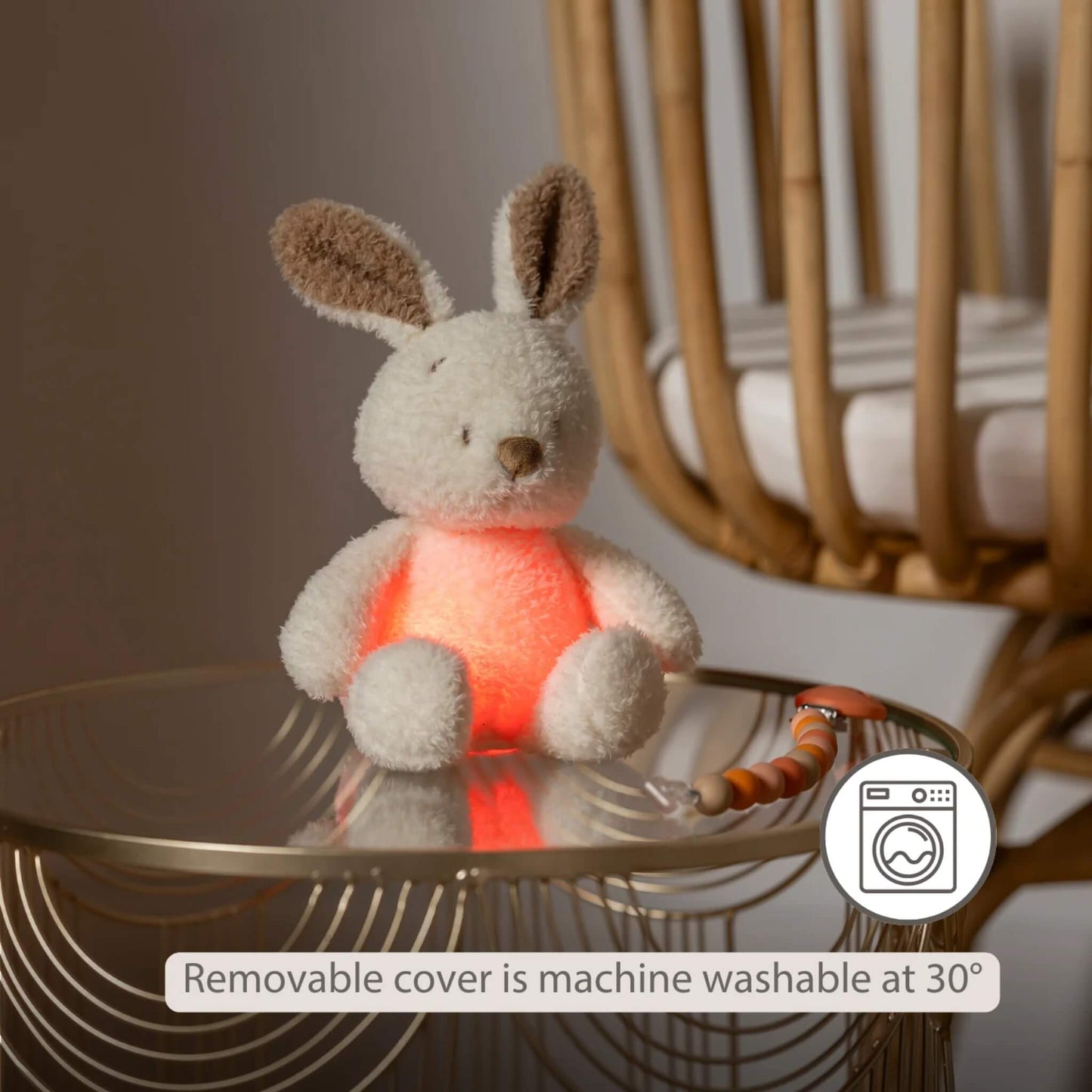 A glowing plush bunny nightlight on a bedside table, with a washing-machine icon indicating the removable cover is machine washable.