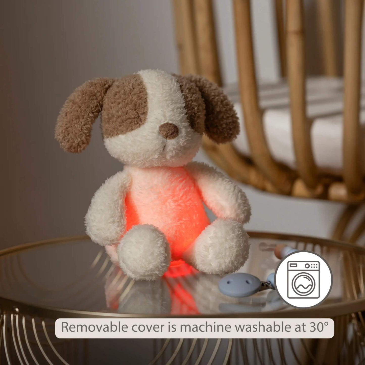 A plush dog nightlight glowing softly in a red tone on a bedside table, with an icon indicating the removable cover is machine washable.