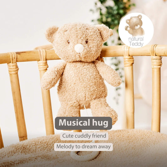 A fluffy teddy bear musical toy hanging from a wooden cot rail with a pull-cord ring below. On-image text reads “Musical hug”, “Cute cuddly friend” and “Melody to dream away”.