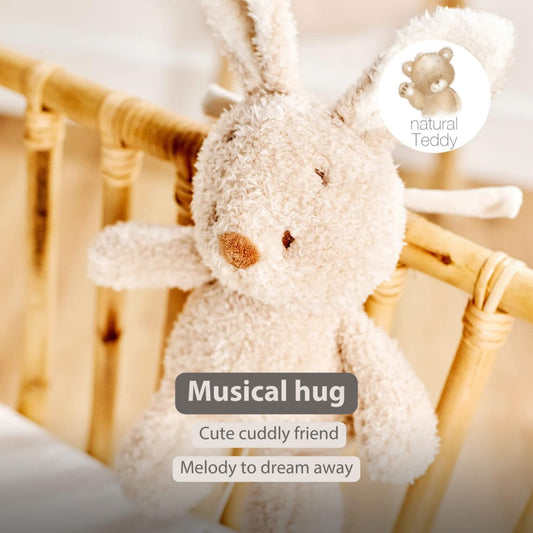A soft bunny musical toy hanging from a wooden cot rail with long ears and plush fur. On-image text reads “Musical hug”, “Cute cuddly friend” and “Melody to dream away”.