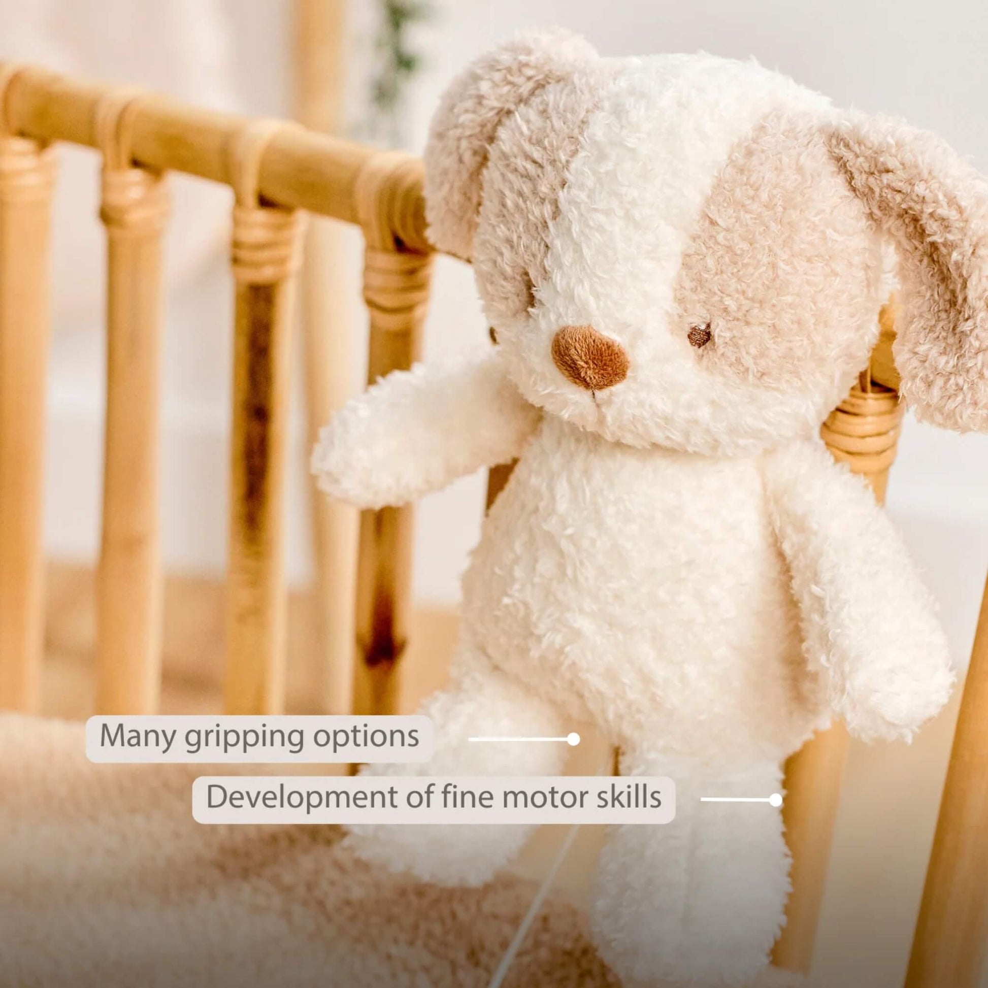 A plush dog musical toy rests against a cot rail with its floppy ears and soft limbs visible, alongside on-image text saying “Many gripping options” and “Development of fine motor skills.”