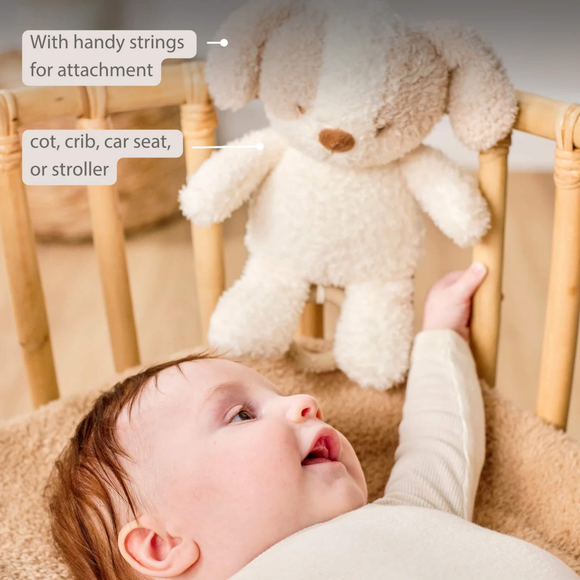 A plush dog musical toy is tied to a cot rail while a baby reaches toward it, with on-image text reading “With handy strings for attachment” and “cot, crib, car seat, or stroller.”