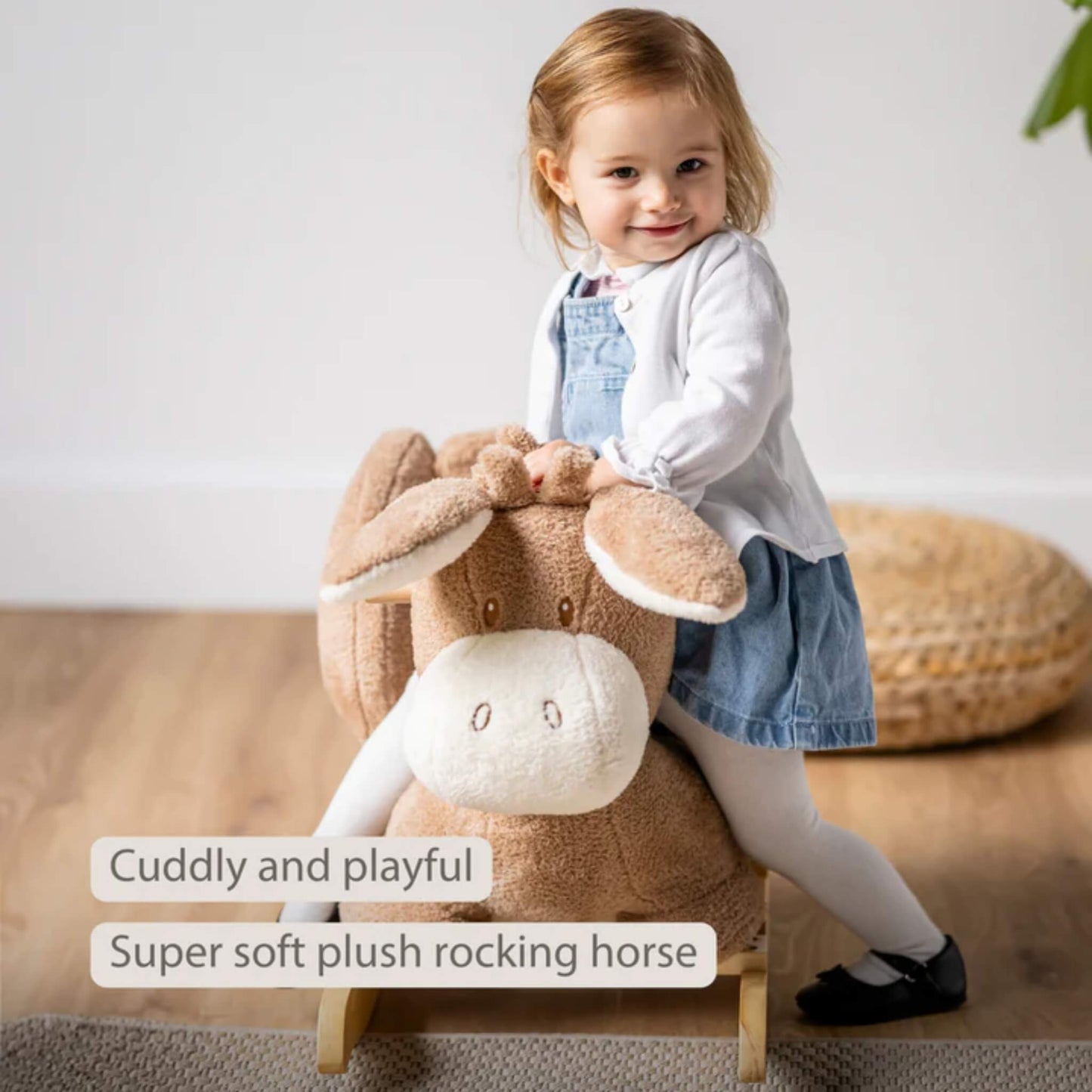 Smiling toddler getting on a padded plush rocking donkey with wide seat and supportive sides in a bright nursery setting.