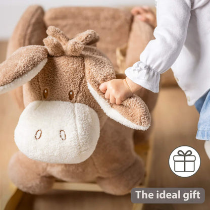 Close-up of a child’s hand gripping a soft plush donkey ear while sitting on a rocking toy in a warm home interior.