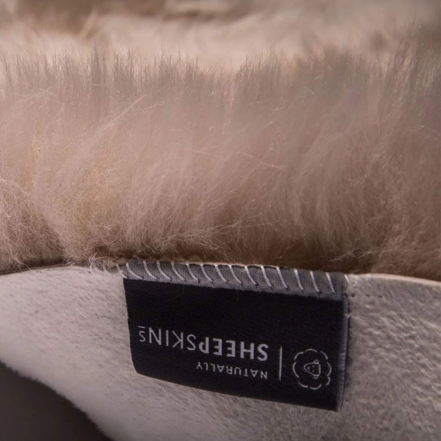 Detailed close-up of the suede backing and stitched label on the grey sheepskin pram liner.