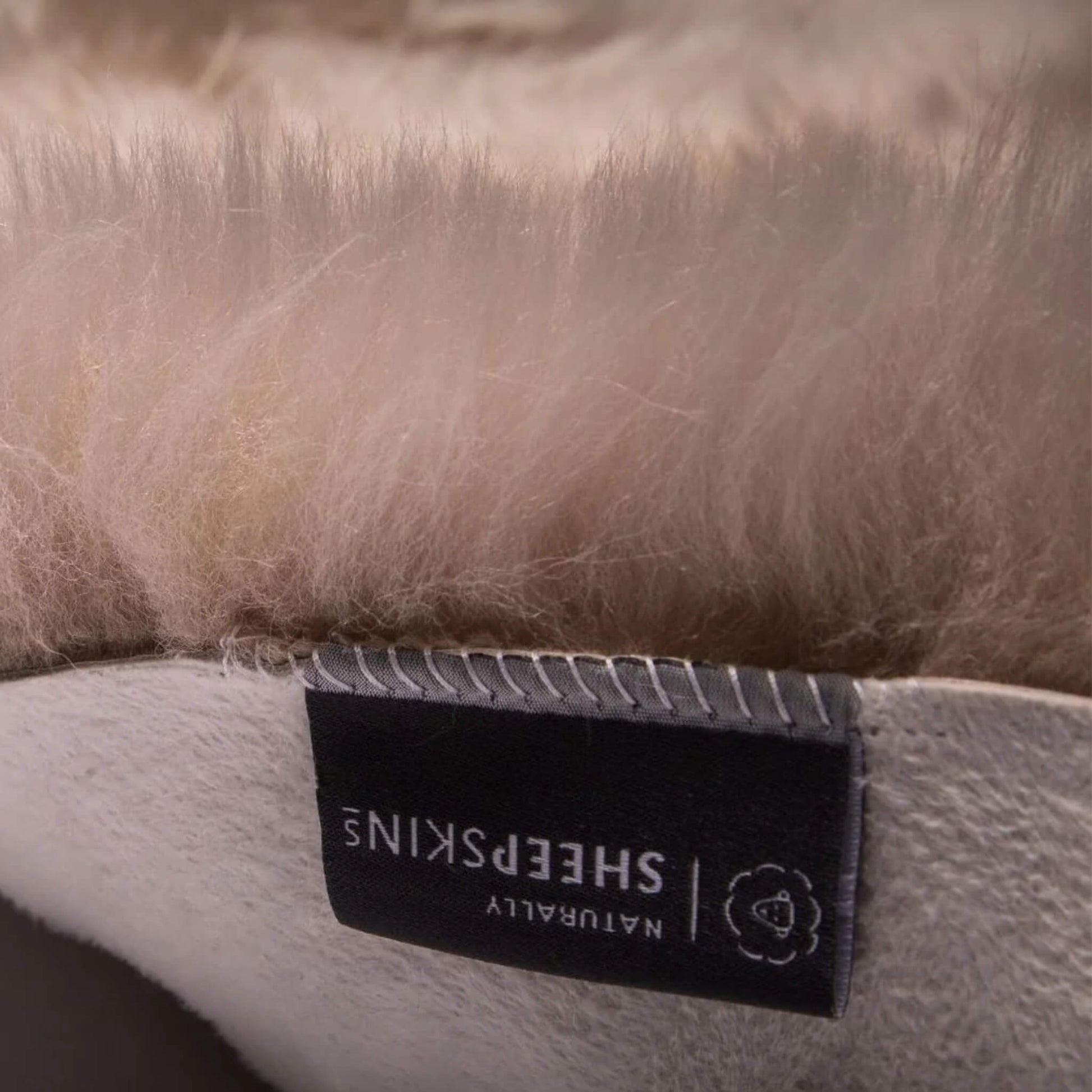 Detailed close-up of the suede backing and stitched label on the grey sheepskin pram liner.
