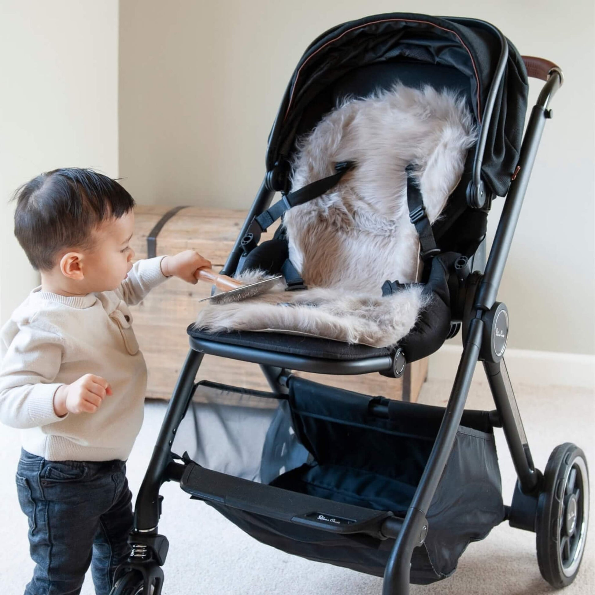Young child brushing the fluffy grey sheepskin liner inside a black pushchair.