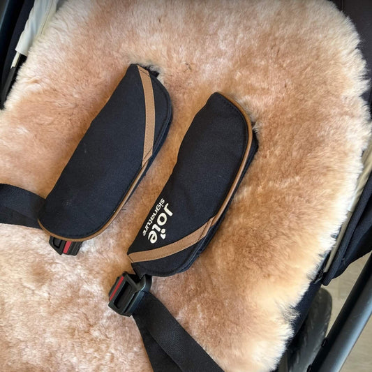 Close-up of a pushchair harness with black padding resting against the soft rose gold sheepskin liner.