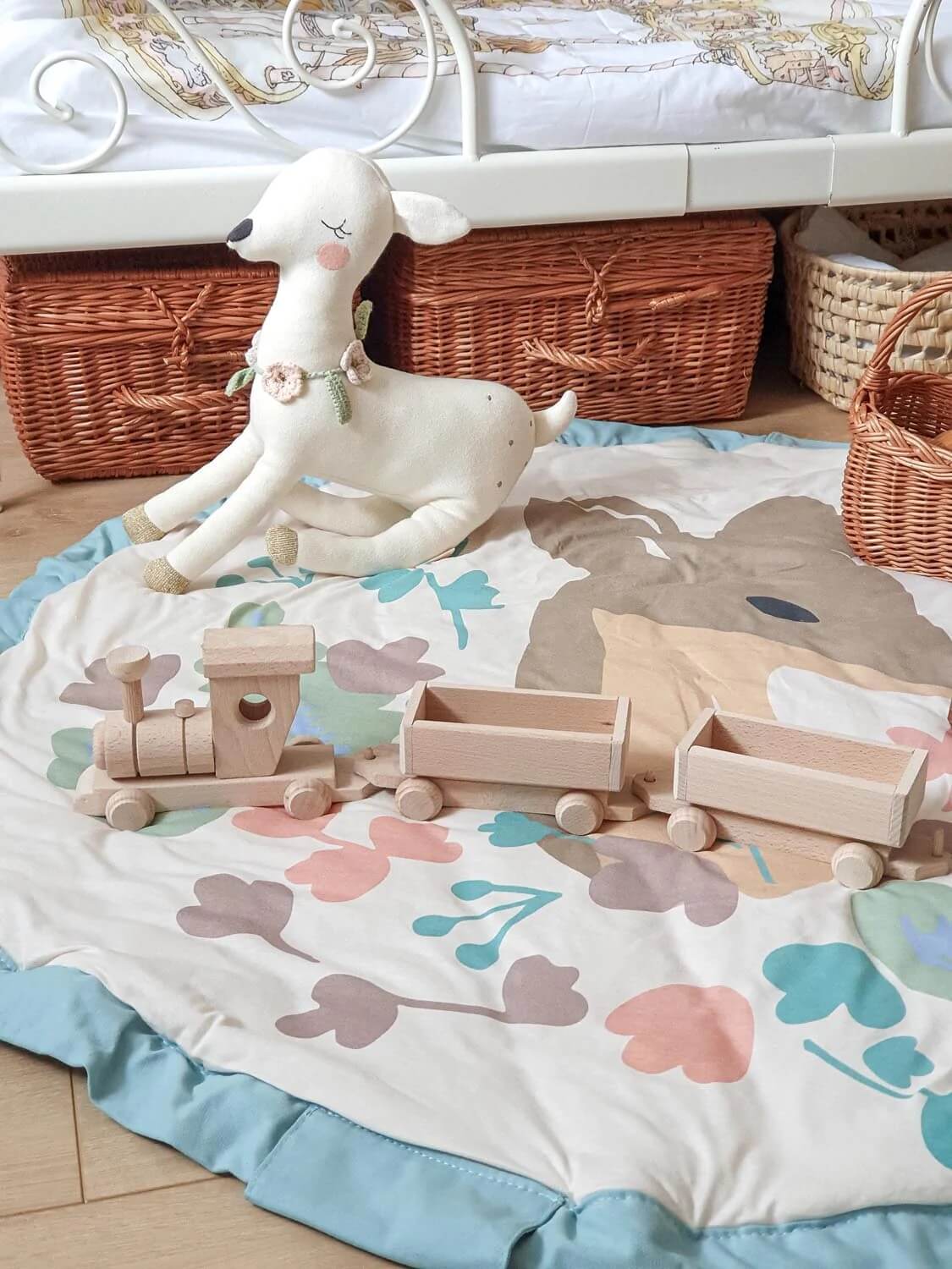 A play mat laid out on a wooden floor with wooden train toys and a soft toy placed on top, showing scale and everyday use.