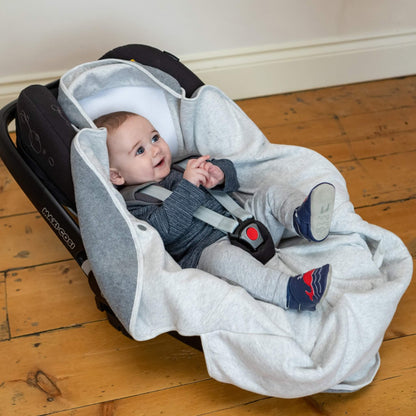 Baby seated in a car seat with light grey hooded fabric positioned around the head and grey fleece panels resting over the legs.