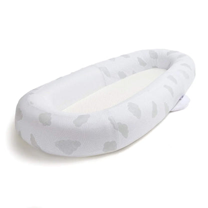 An angled view of a baby bed showing the oval shape and gently structured sides surrounding a flat sleep surface.