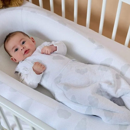 A baby lying on their back inside a padded baby bed with raised sides and a breathable mesh base.