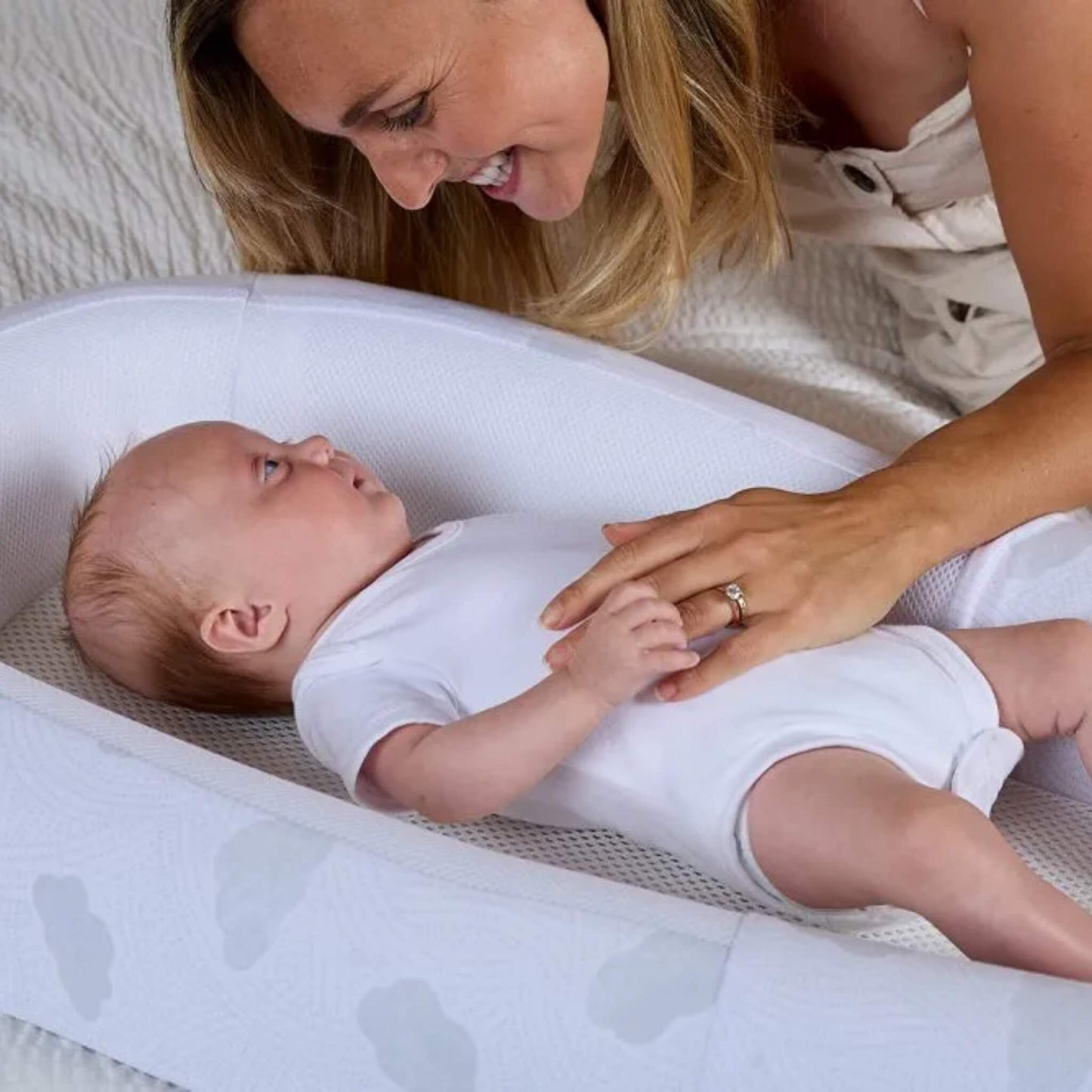 An adult leaning over a baby lying in a padded baby bed, showing scale and depth of the cushioned sides.