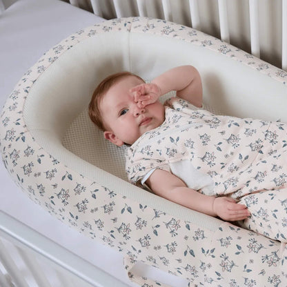 A side view of a baby bed showing raised, structured sides with a soft floral fabric finish.