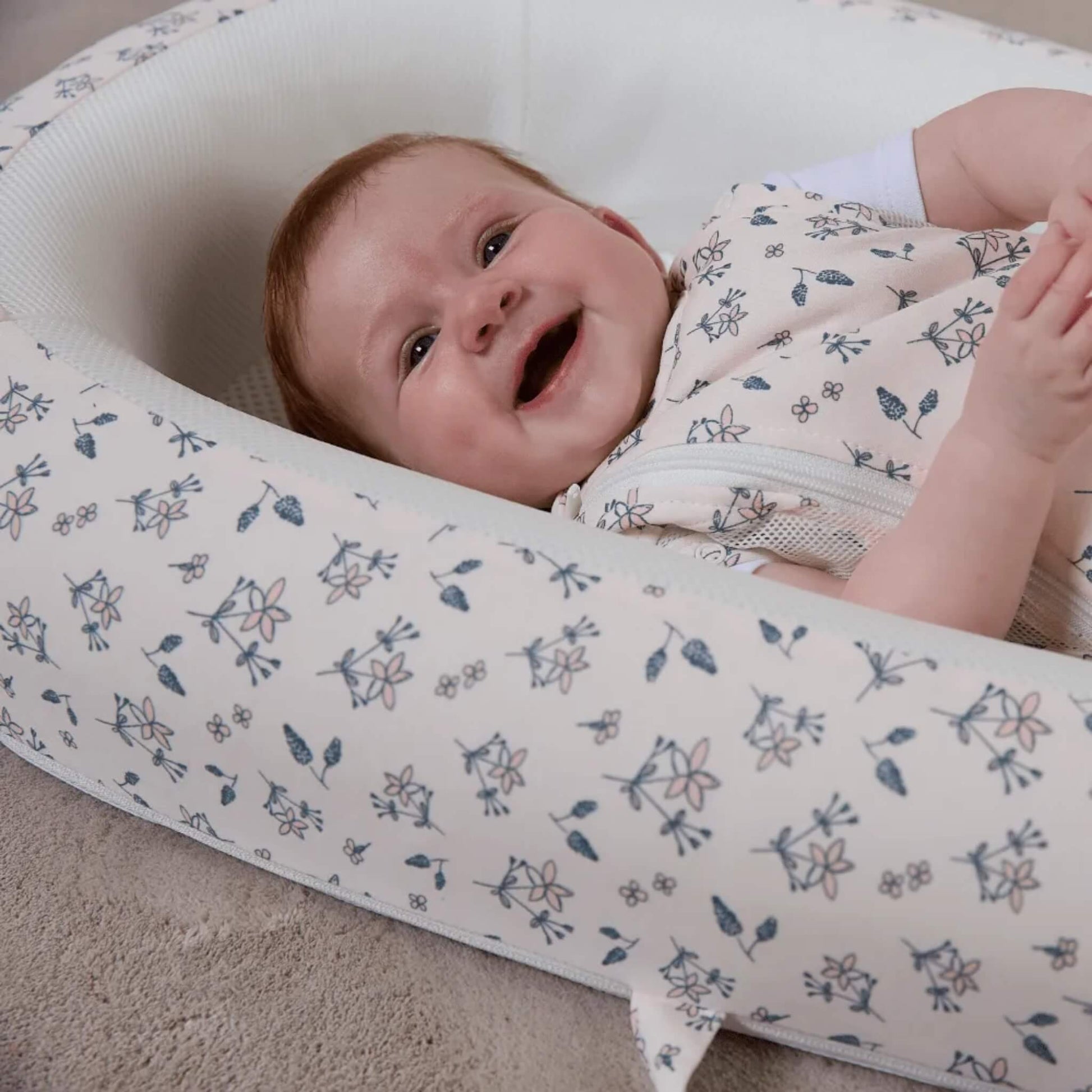A close-up of a smiling baby lying on a mesh mattress surrounded by softly structured sides.