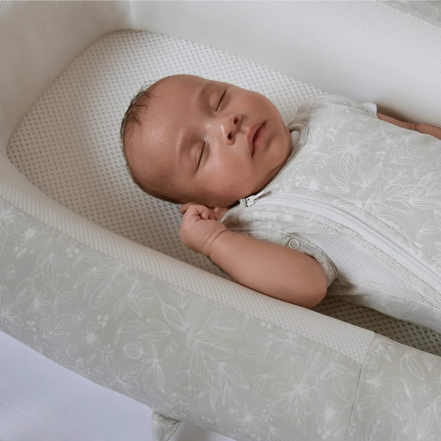 A newborn baby resting inside a baby bed, lying on a breathable mesh base with supportive sides around the body.