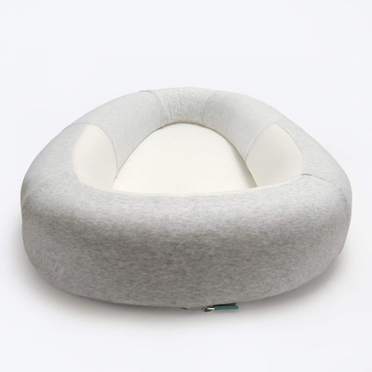 A structured baby bed in soft grey fabric, shown from a low front angle to highlight the cushioned outer shape and mesh sleeping surface.