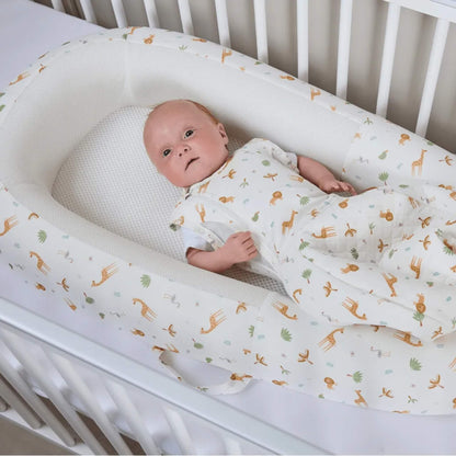 A baby resting inside a baby bed placed on a cot mattress, showing the depth of the sides and the flat mesh sleep surface.