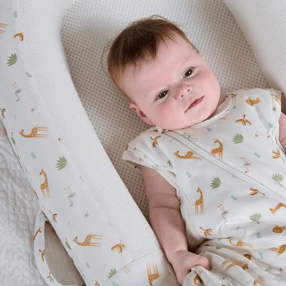 A close-up of a baby lying inside a structured baby bed, highlighting the breathable mesh base and safari animal print fabric.