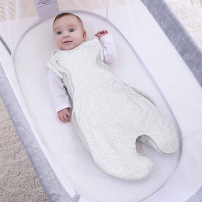 A baby lying awake in a grey swaddle sleep bag with arms out, showing the option to transition from swaddling as baby grows.
