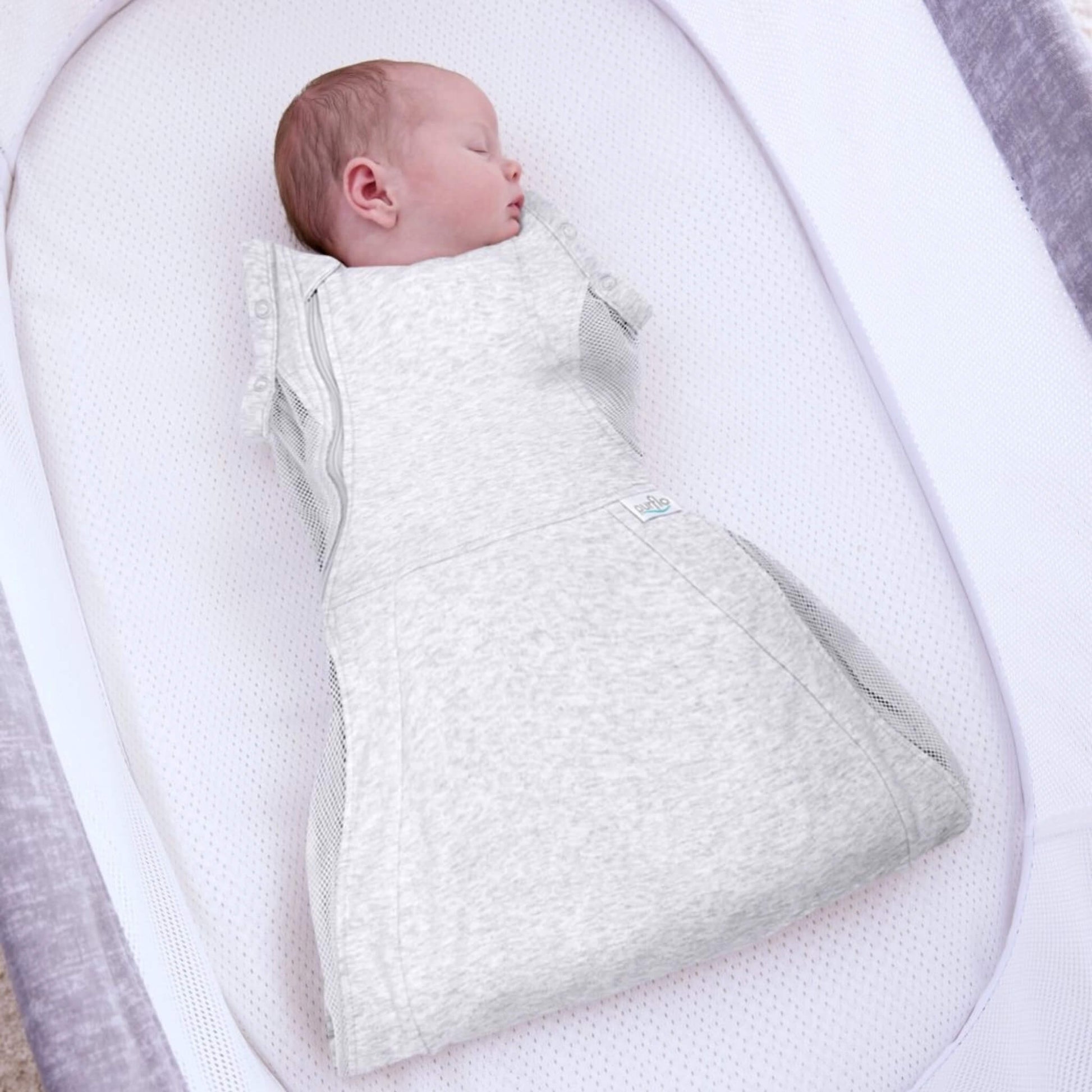 A baby sleeping in a grey swaddle sleep bag inside a breathable bassinet, with mesh panels visible along the sides.