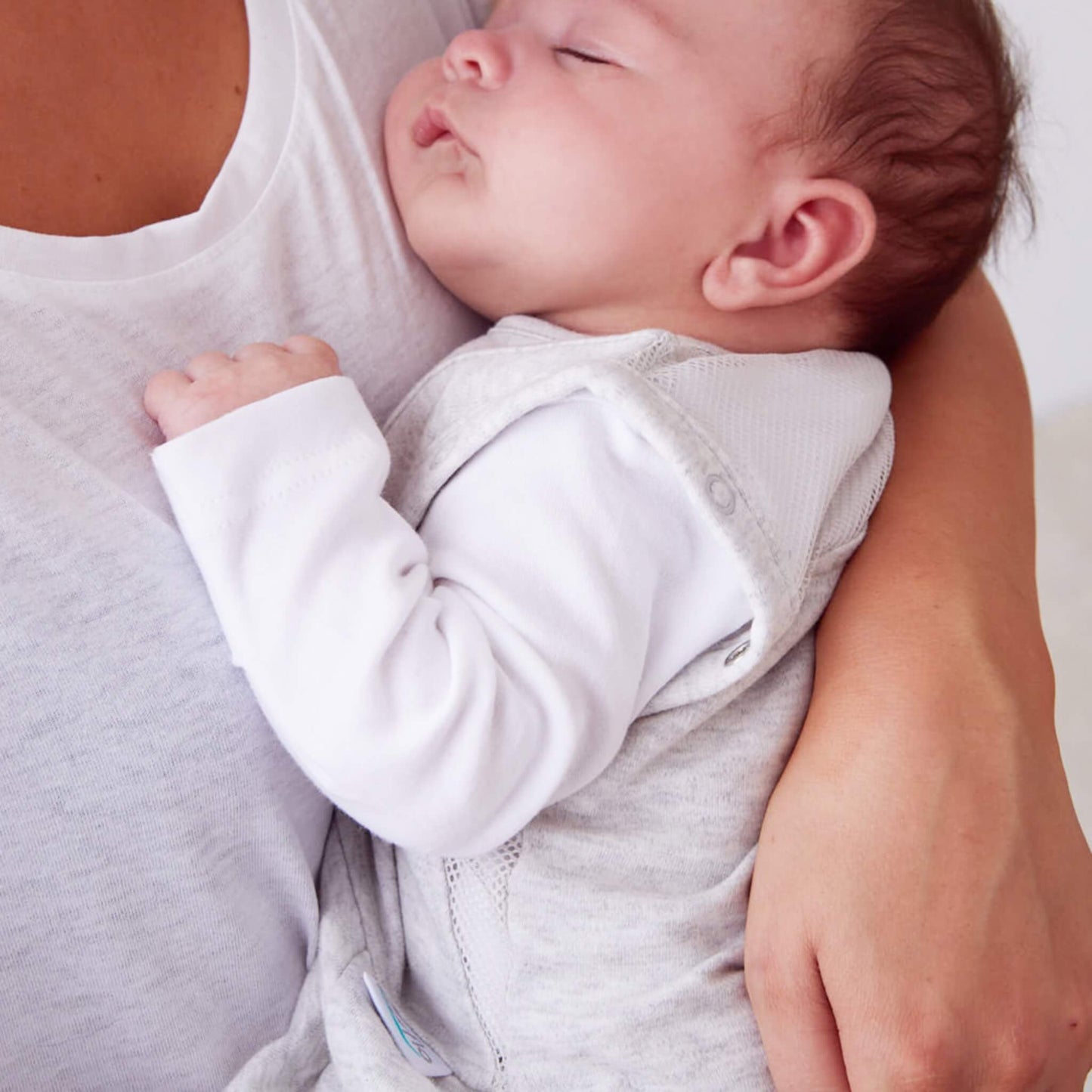 A detailed view of a baby sleeping while held, highlighting the soft fabric and ventilated shoulder area of the sleep bag.