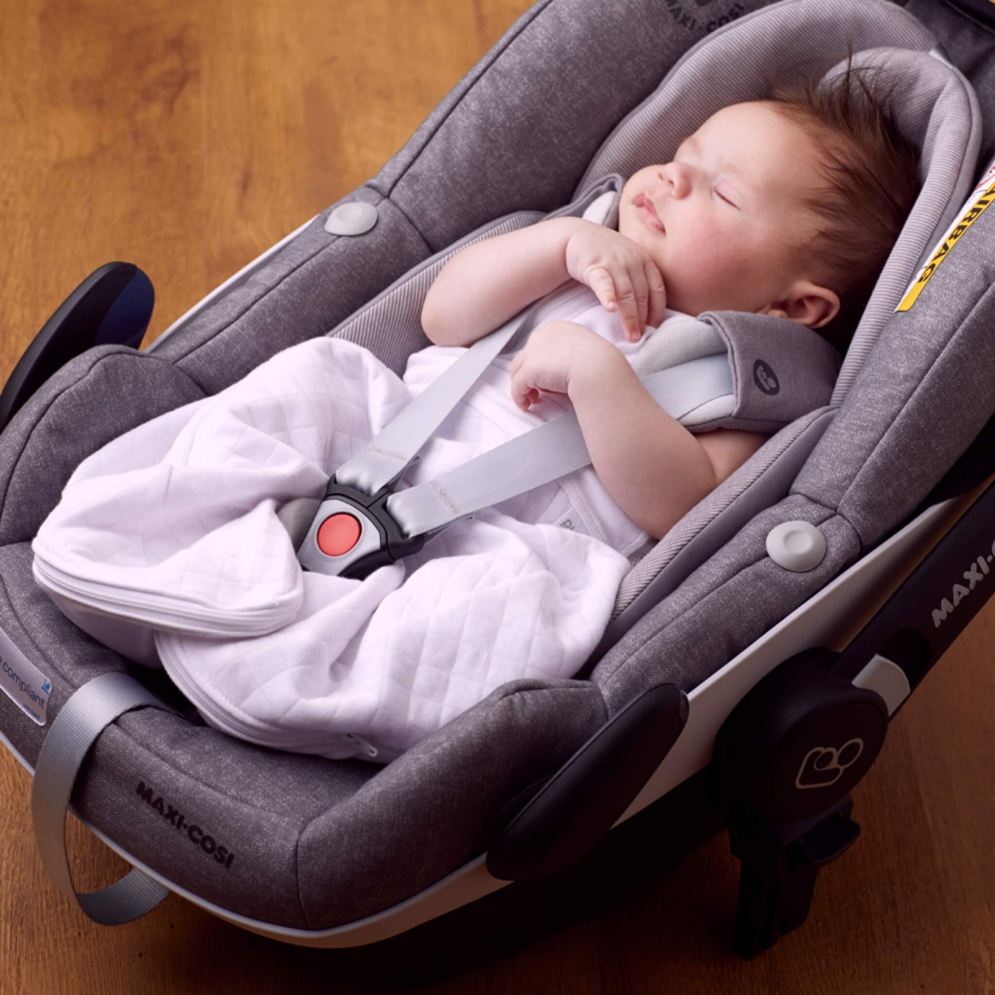 A baby sleeping in a car seat while wearing a lightweight swaddle sleep bag, showing compatibility with travel harnesses.
