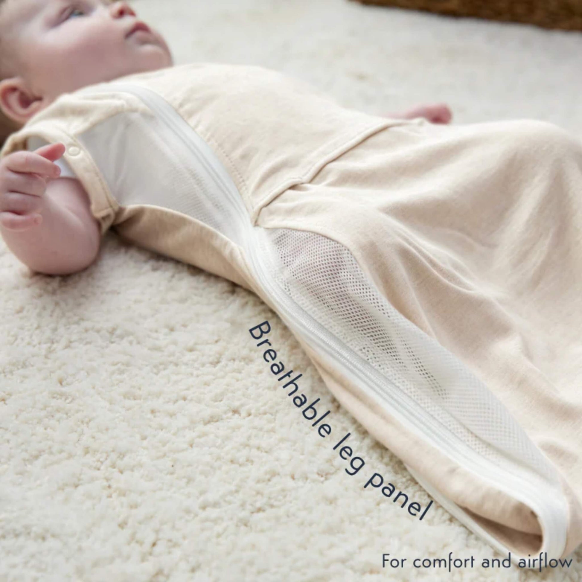 A baby lying comfortably in the Summer Sand swaddle bag with the breathable mesh side panel visible.