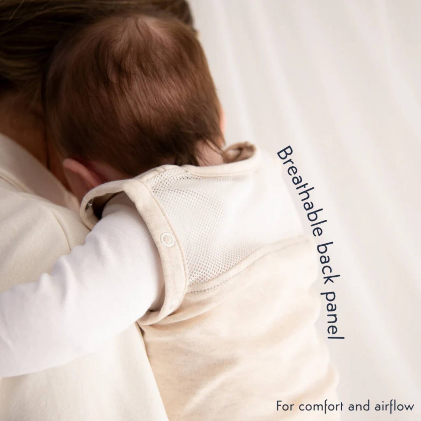 A close-up of a baby being held on an adult's shoulder, showing the breathable mesh back panel of the swaddle bag.