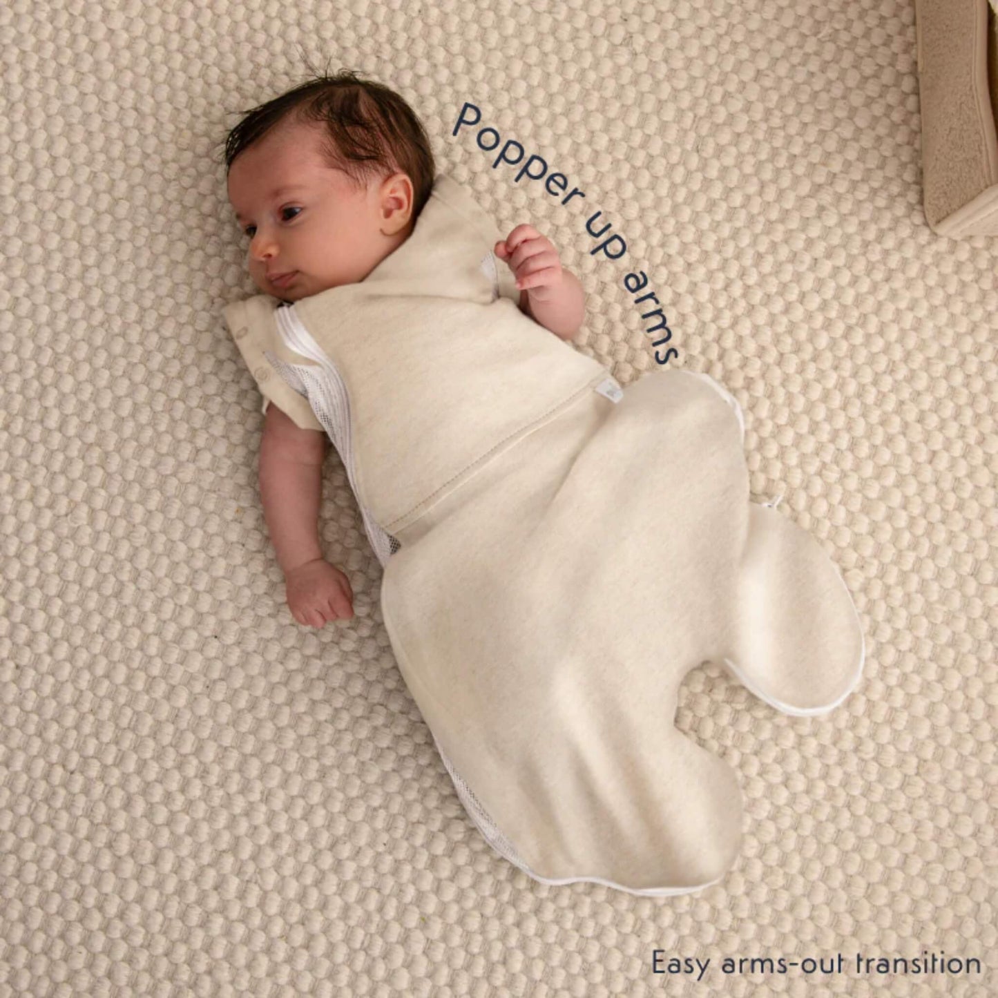 A baby wearing the swaddle bag with arm released through the popper opening during the transition to arms-out sleeping.