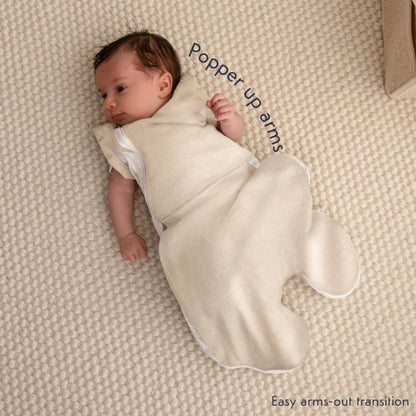 A baby wearing the swaddle bag with arm released through the popper opening during the transition to arms-out sleeping.
