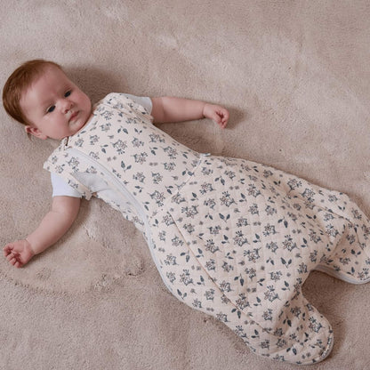 A baby lying on a soft carpet wearing a swaddle to sleep bag with arms out, showing the transition from swaddling to a standard sleep bag.