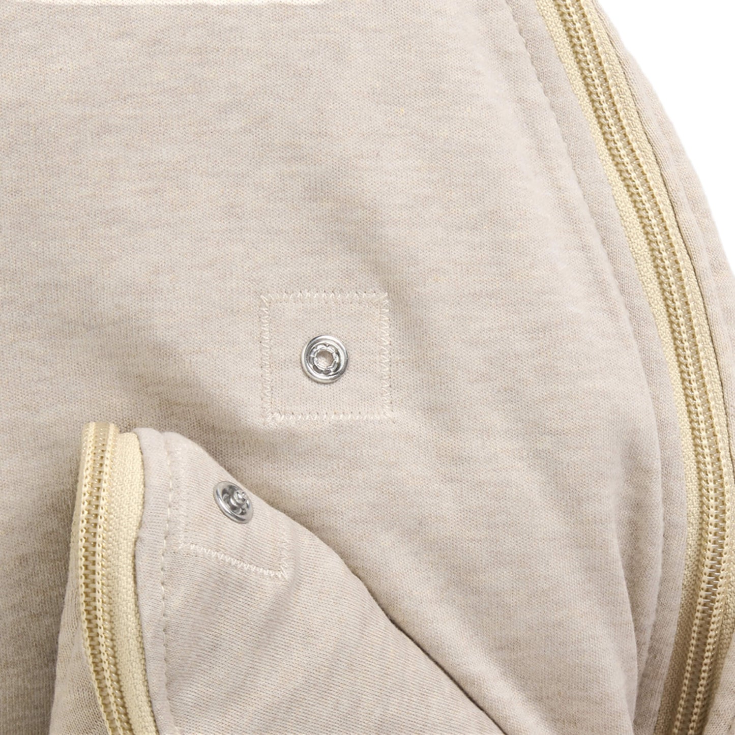 A close-up of a press stud fastening on a beige baby sleep bag.