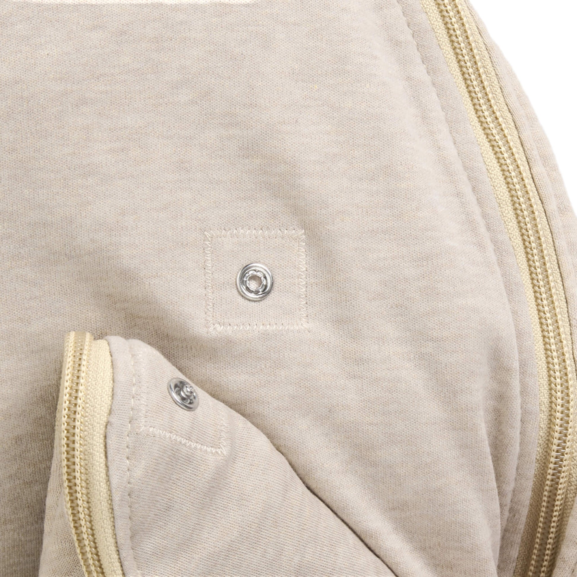 A close-up of a press stud fastening on a beige baby sleep bag.