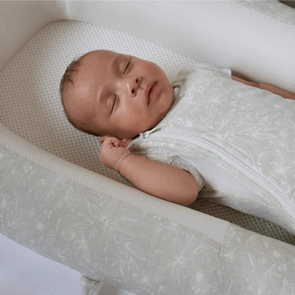 A close-up of a sleeping baby in a swaddle sleep bag, highlighting the curved zip, mesh side panel, and snug fit around the torso.