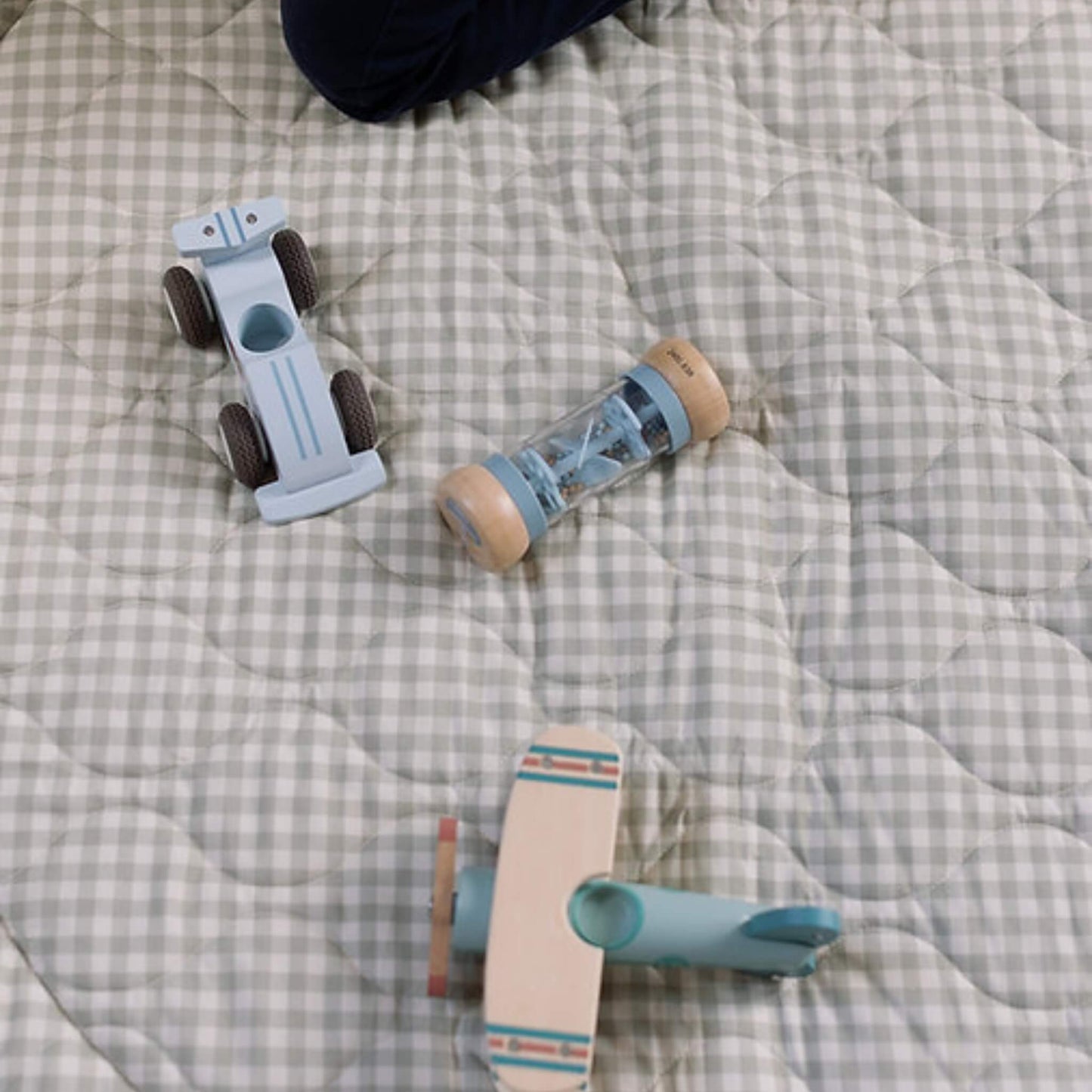 Wooden toy car, rattle and small plane placed on a soft quilted gingham play mat, showing texture and stitched pattern in detail.