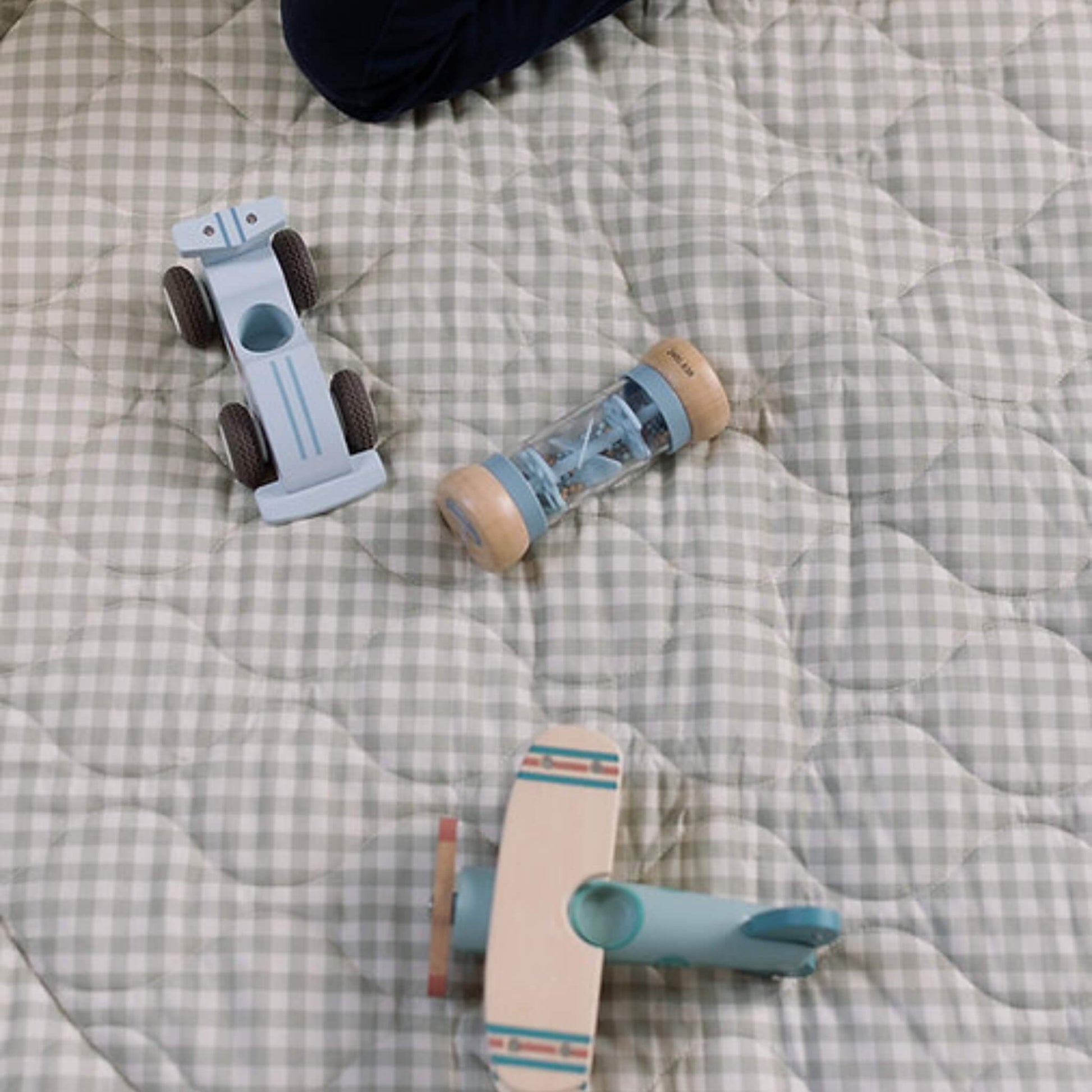 Wooden toy car, rattle and small plane placed on a soft quilted gingham play mat, showing texture and stitched pattern in detail.