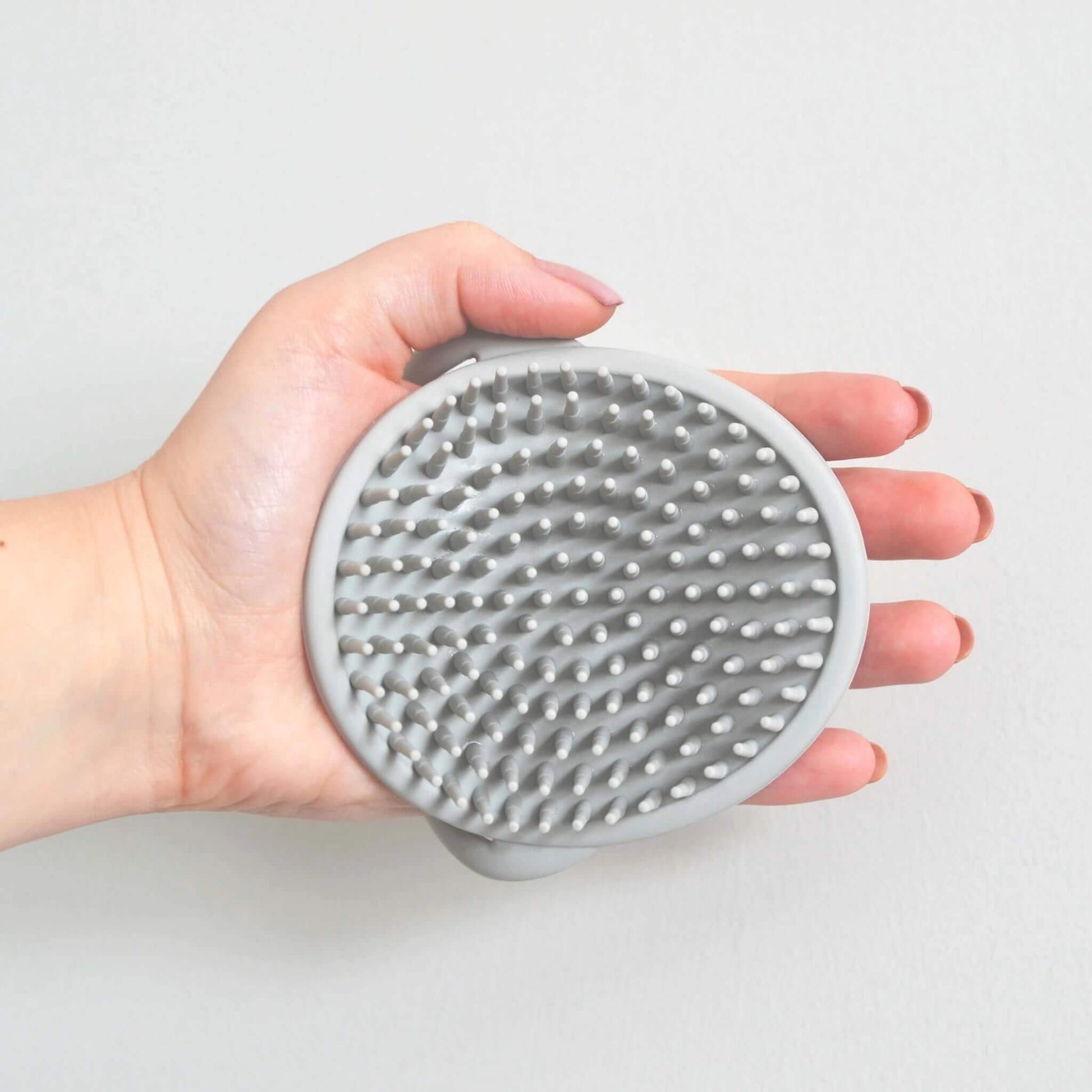 A top-down view of a grey silicone baby bath brush resting in a hand, showing dense, rounded bristles for gentle cleansing.