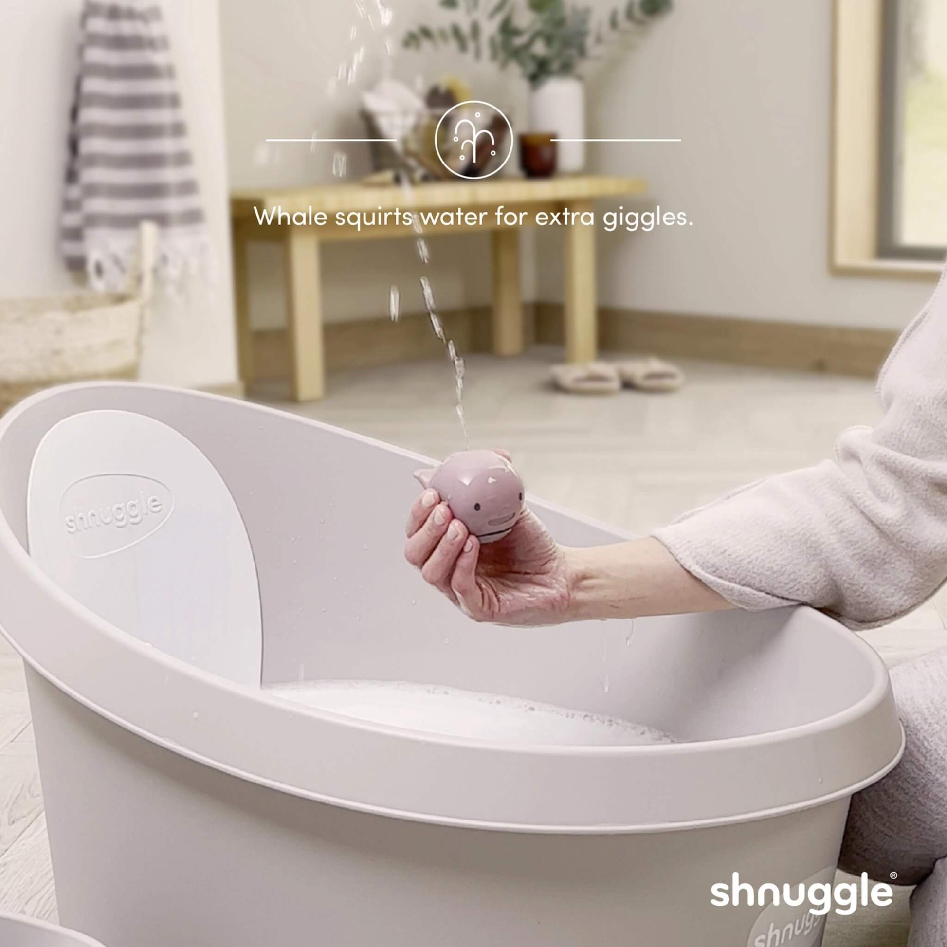 A pale pink whale bath toy held above a bath, with water squirting in a thin stream from the spout.