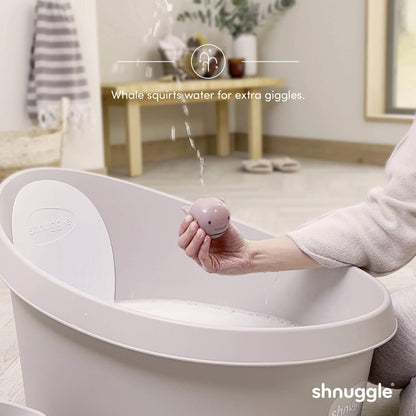 A pale pink whale bath toy held above a bath, with water squirting in a thin stream from the spout.