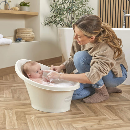 Baby sitting in a foam-filled bath while their mother gently touches the tip of the baby’s nose.