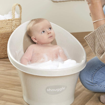 Baby sitting upright in a small bath filled with bubbles, gazing upwards with a curious expression.