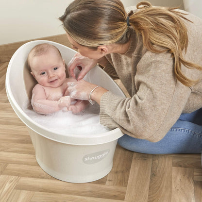 Baby in a bubble-filled bath smiling as their mother leans forward and gently washes them