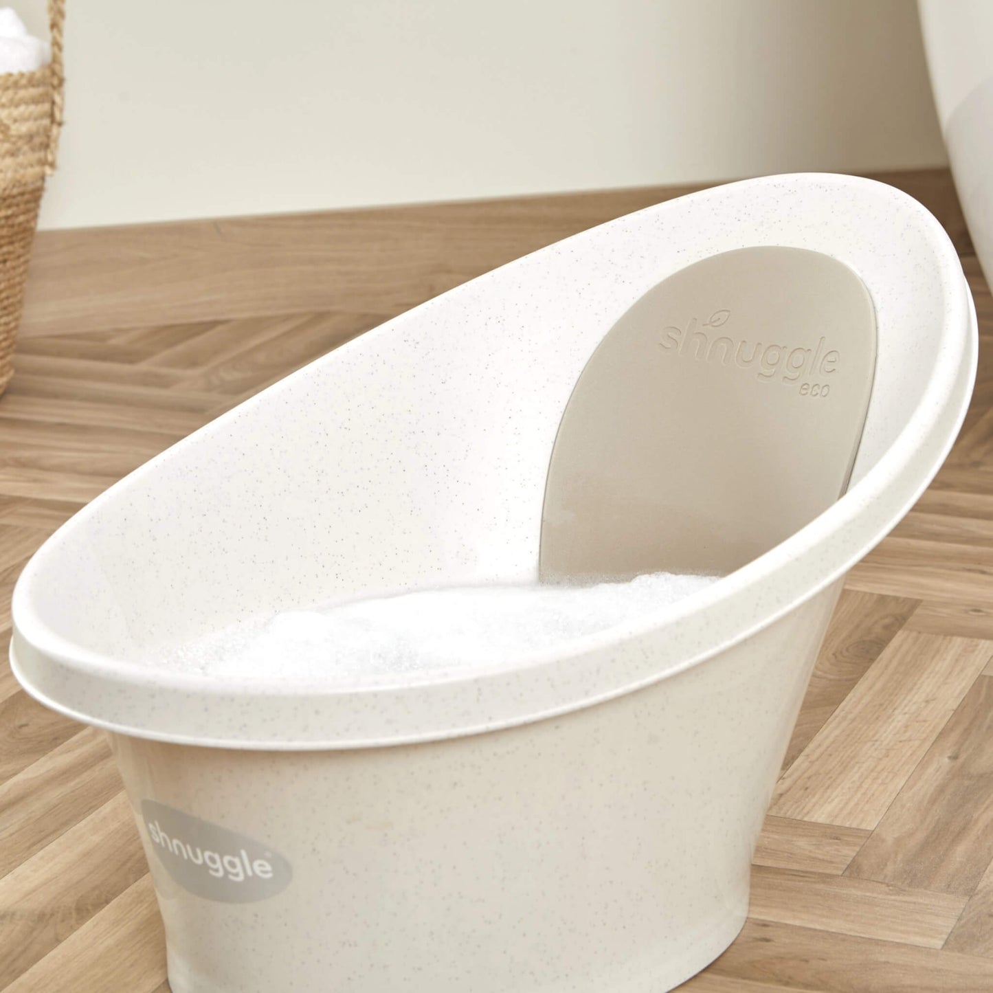 Close-up of a cream-coloured baby bath partly filled with foam, showing its curved backrest and seat.