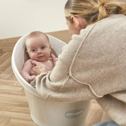 Baby sitting in a bath while their mother supports them with both hands.