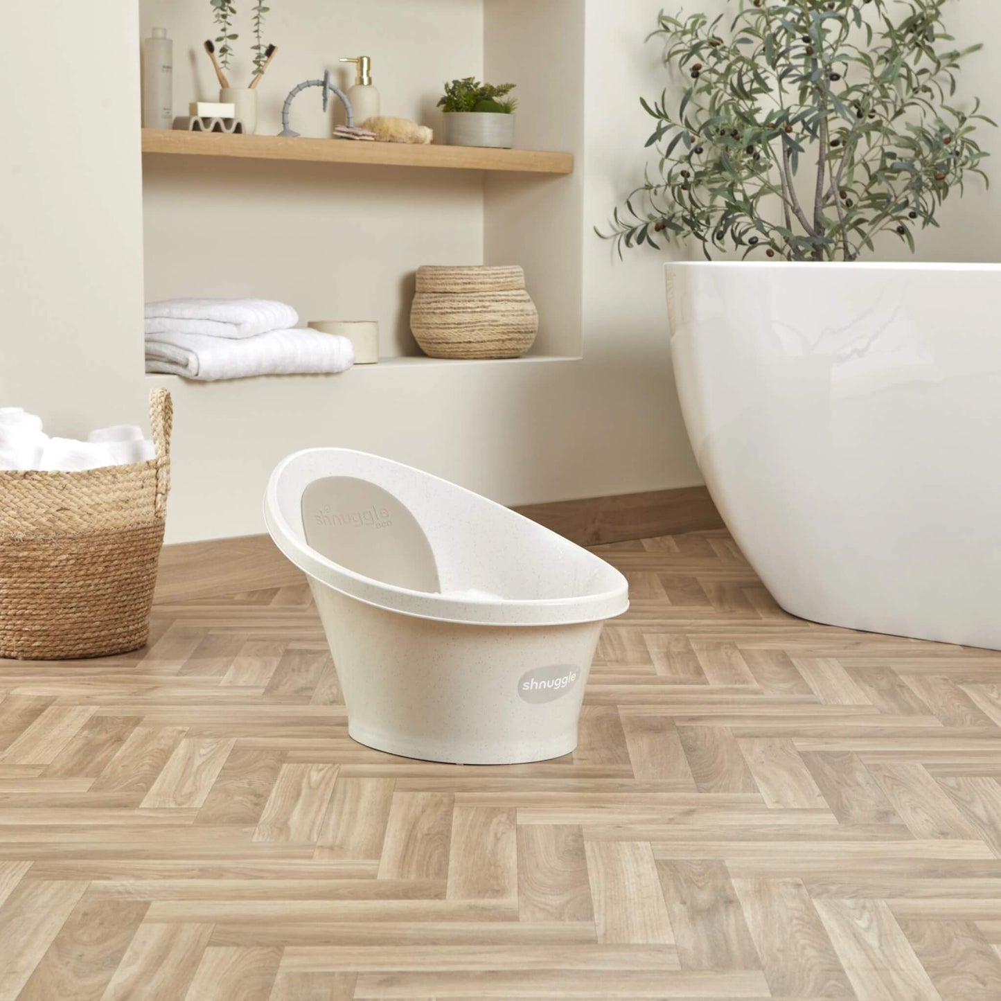 Freestanding cream baby bath positioned on a wooden floor in a modern bathroom setting.